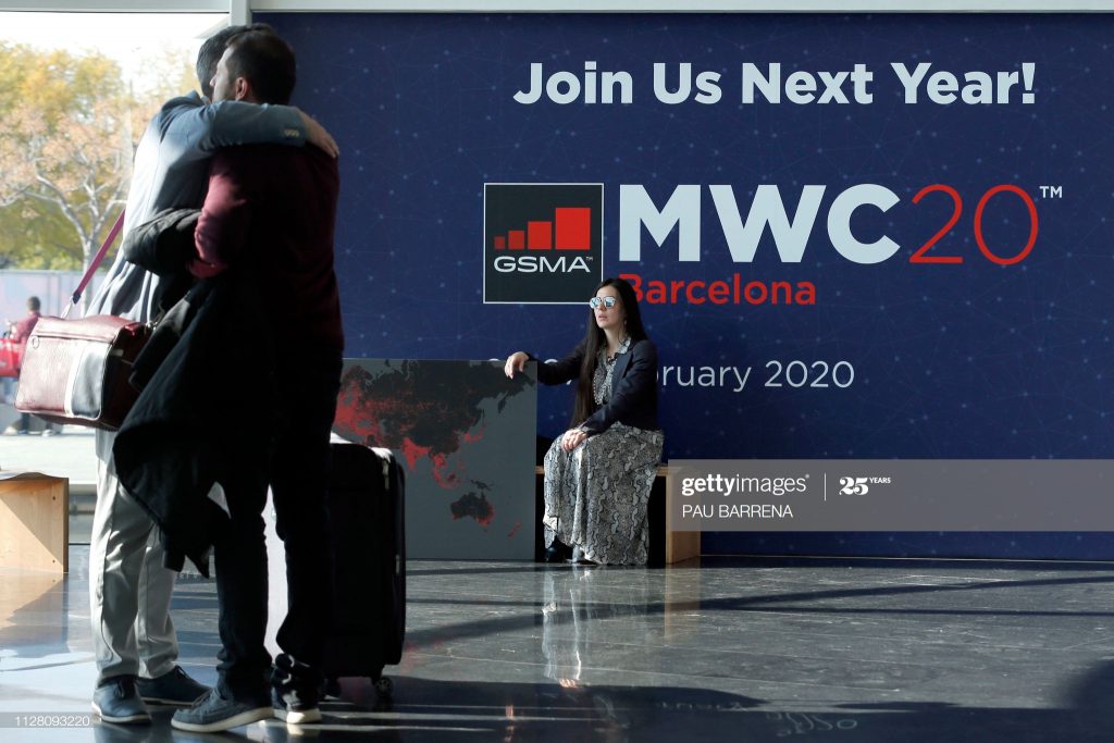A woman looks at two visitors hugging each other on the last day of the Mobile World Congress (MWC) in Barcelona on February 28, 2019. - Phone makers focused on foldable screens and the introduction of blazing fast 5G wireless networks at the world's biggest mobile fair as they try to reverse a decline in sales of smartphones. (Photo by Pau Barrena / AFP) (Photo credit should read PAU BARRENA/AFP via Getty Images)
